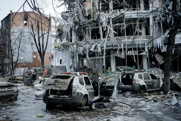Damaged multi-storey building and burned-out cars amid rubble