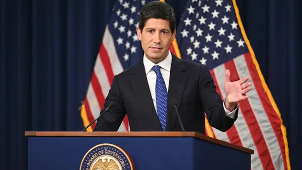 Kevin Warsh speaking at a lectern in front of American flags