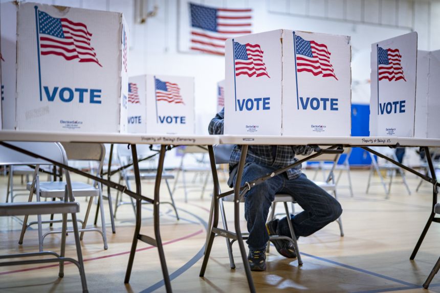Voters casting ballots behind American flag voting booths.
